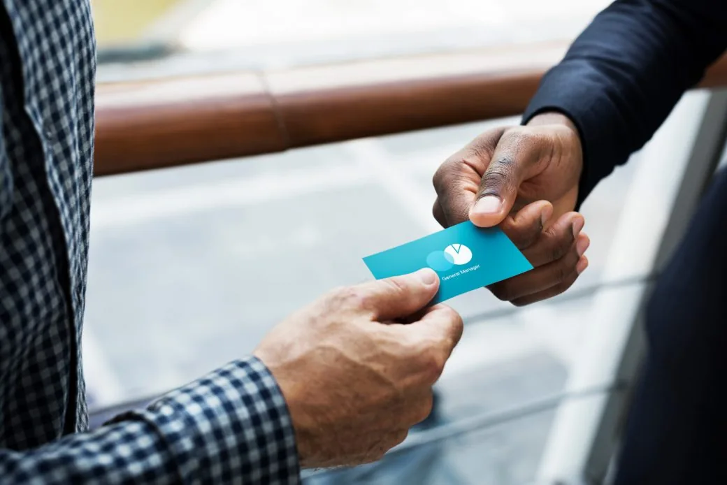 Two people exchanging a business card outdoors on a terrace.
