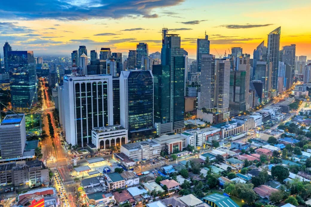 A city skyline at sunset with illuminated skyscrapers and city streets below.