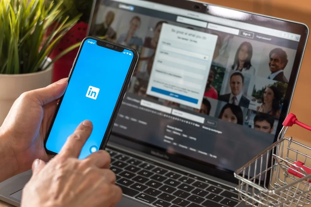 A phone showing the LinkedIn app held in front of a laptop displaying a sign-in page.