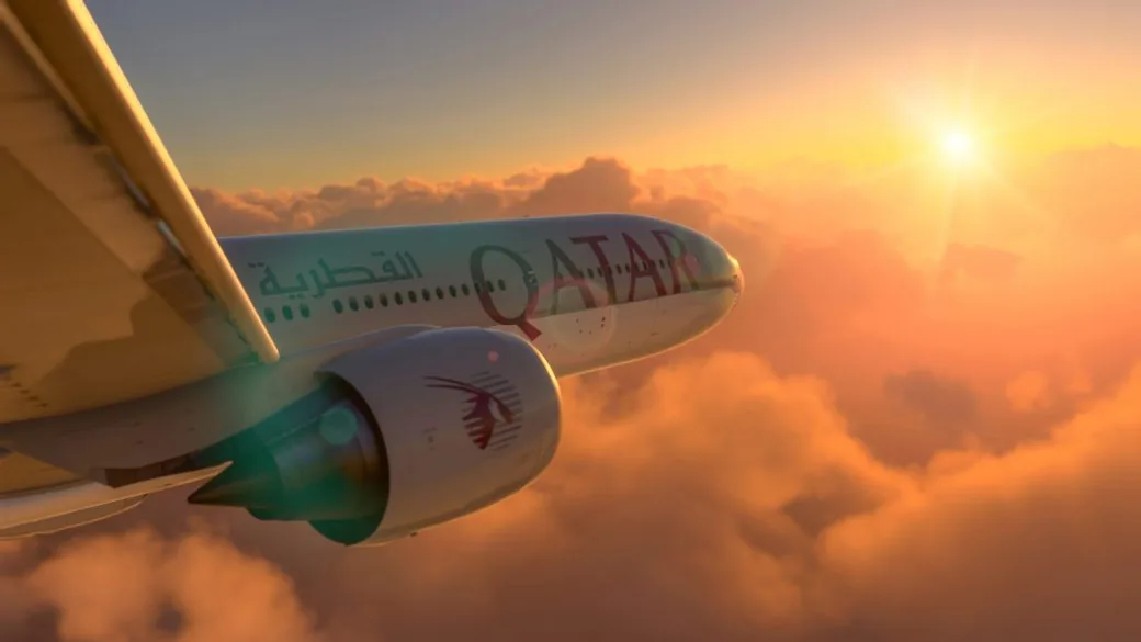 A Qatar Airways aircraft flying above clouds at sunset, seen close on the wing and engine.