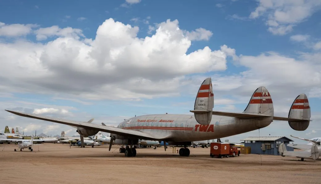 A vintage TWA propeller aircraft parked on an airfield under a partly cloudy sky.