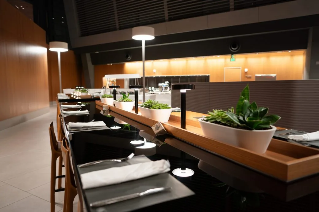 An airport lounge dining counter set with cutlery, napkins and small potted plants.