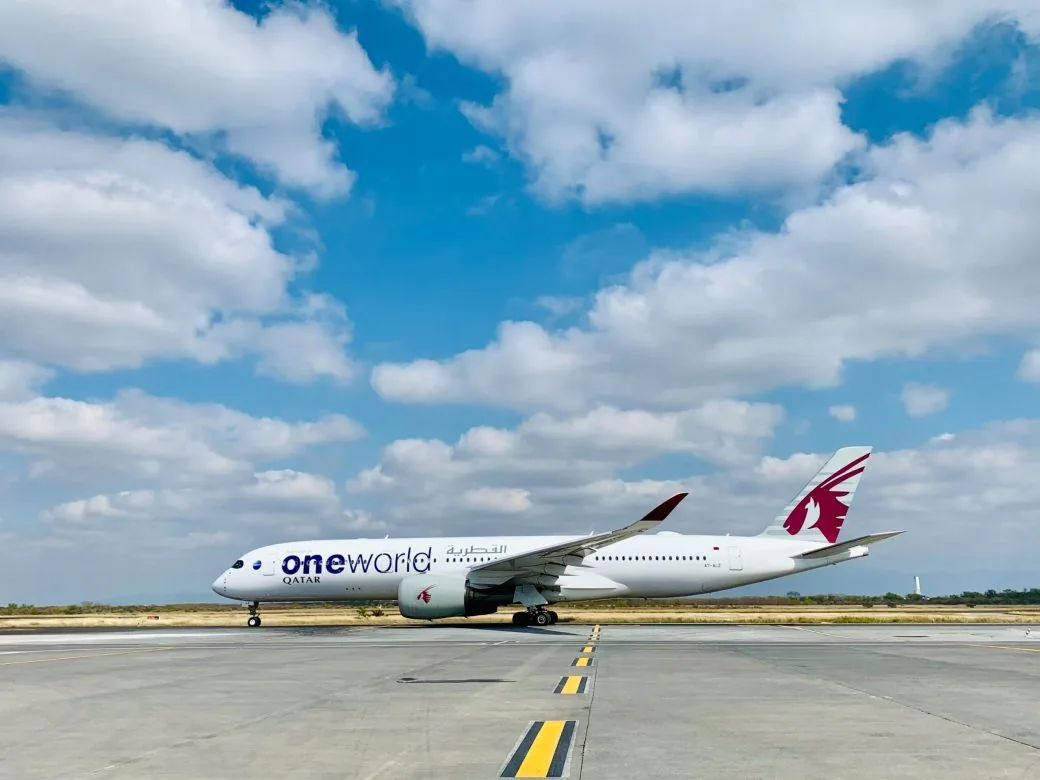 An aircraft in Qatar Airways livery taxiing on an airport runway under a partly cloudy sky.