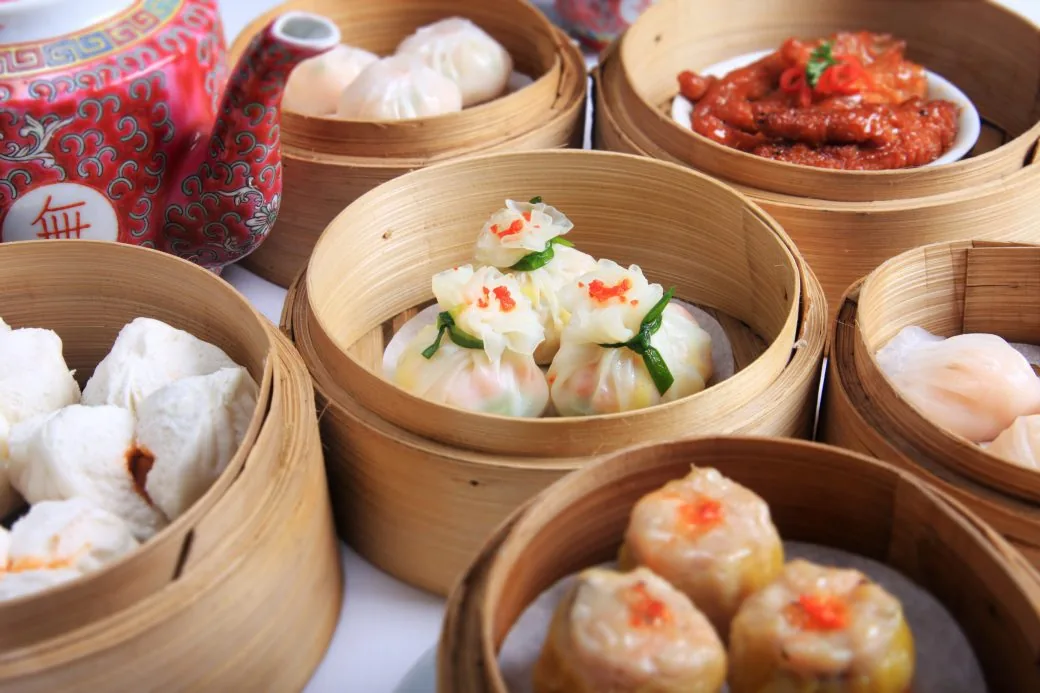 Assorted dim sum in bamboo steamer baskets alongside a patterned teapot.