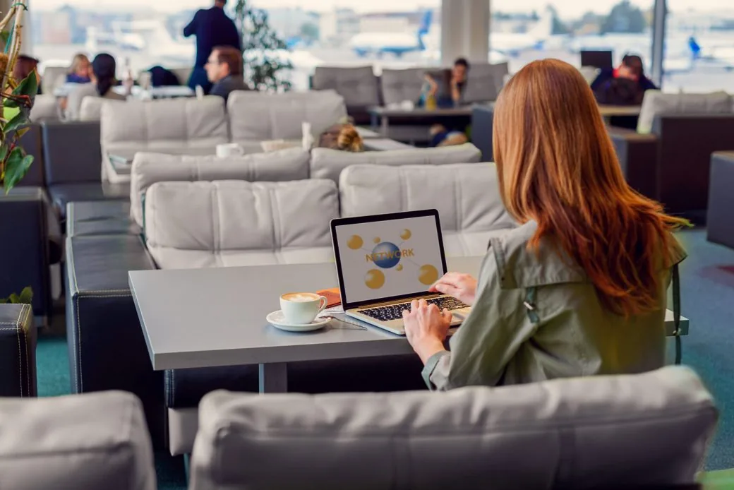A traveller working on a laptop beside a coffee in an airport lounge seating area.