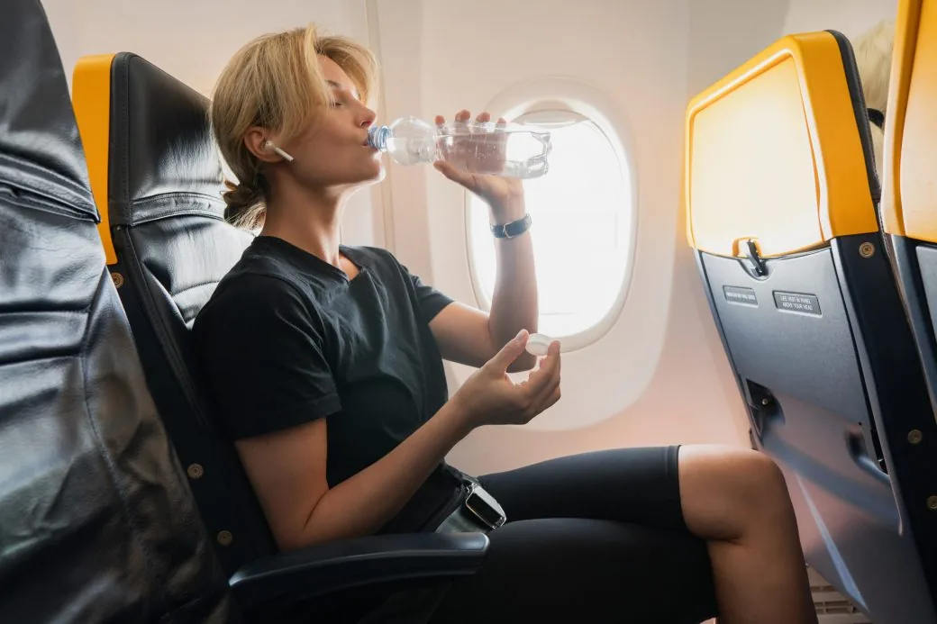 A passenger drinking bottled water in an aircraft window seat.