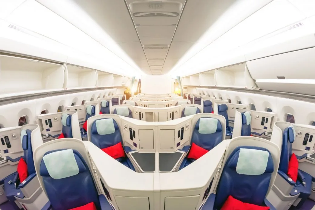 Rows of empty business class aircraft seats with red pillows and blue upholstery.