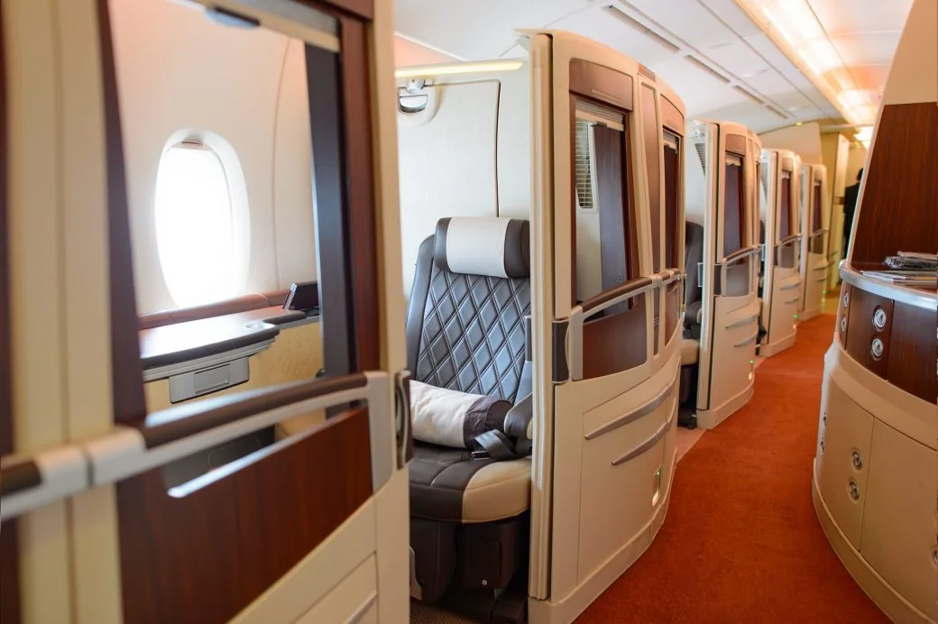 A row of enclosed first class suites with wooden doors along an aircraft aisle with orange carpet.