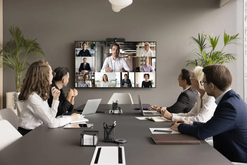 A team in a boardroom taking part in a video call with colleagues shown on a wall screen.
