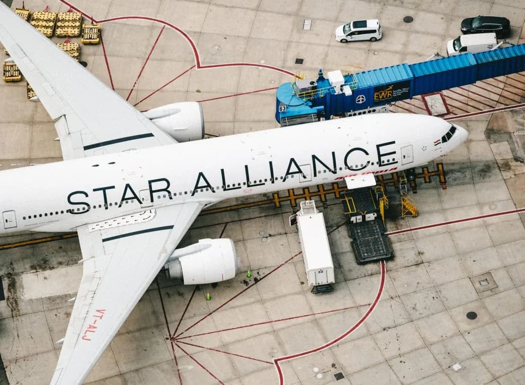 An aircraft in Star Alliance livery on the tarmac, seen from above with ground vehicles nearby.