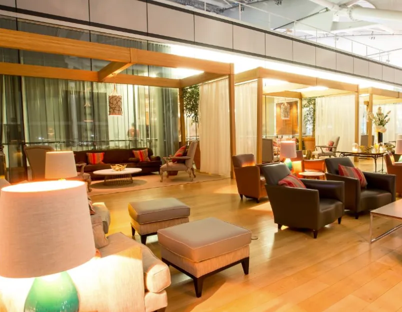 A lounge seating area with sofas, armchairs and warm lamplight beneath wood-beamed partitions.